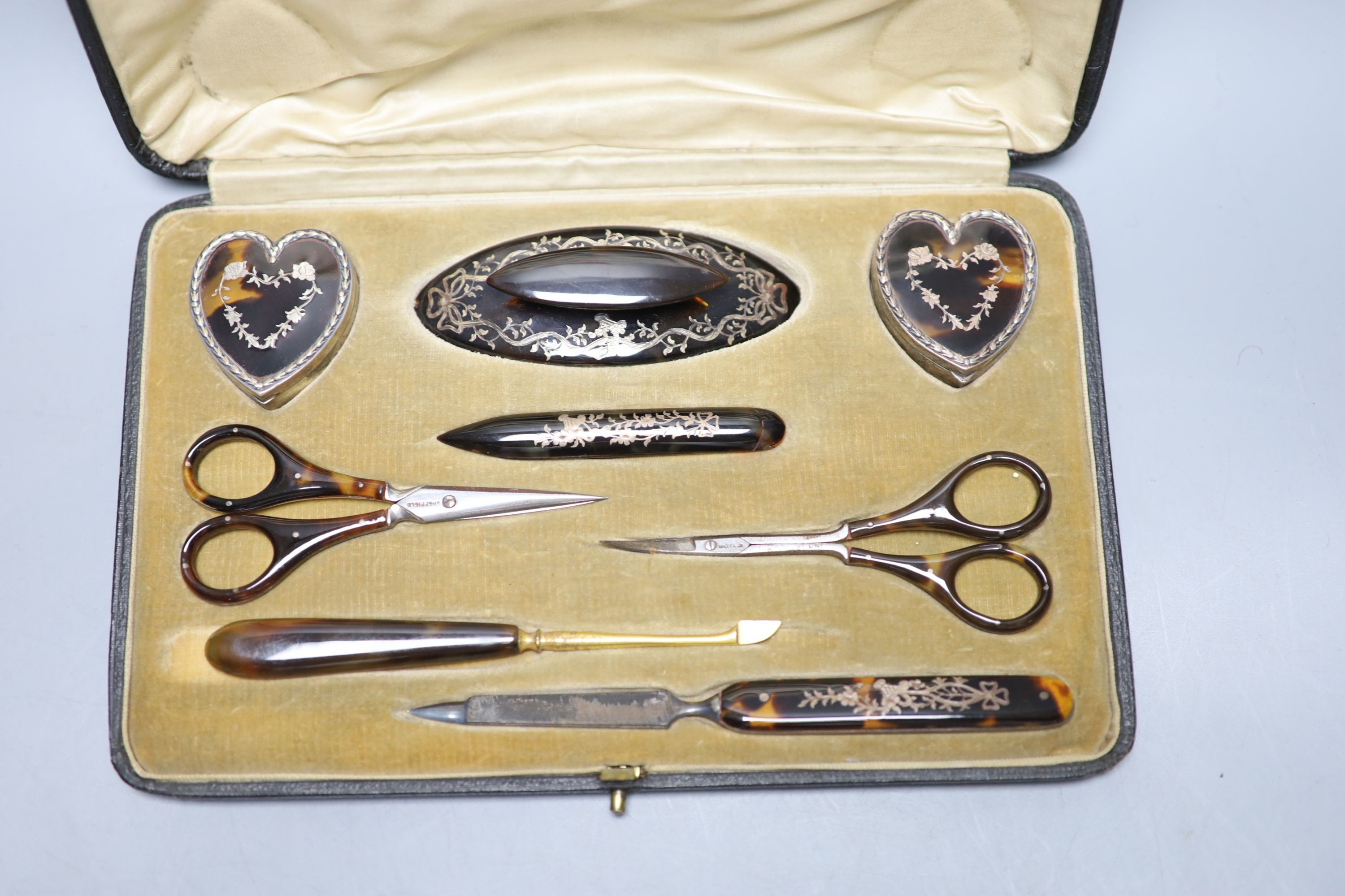 A cased Edwardian eight piece tortoiseshell pique necessaire (one piece replaced), including two silver mounted heart shaped boxes, Birmingham, 1906.